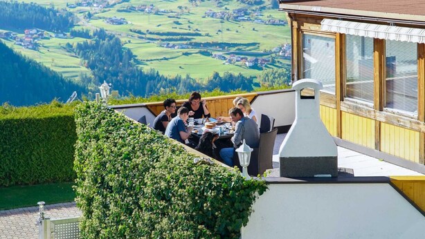 A group of people dining at an outdoor table with a scenic view of a valley.