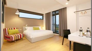 Ein modernes Hotelzimmer mit einem Bett, einem gestreiften Sessel, einem Schreibtisch mit Wasserflaschen und einem großen Fenster.