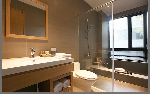 Un baño moderno con ducha envuelta en vidrio, tocador de madera y un espejo grande.