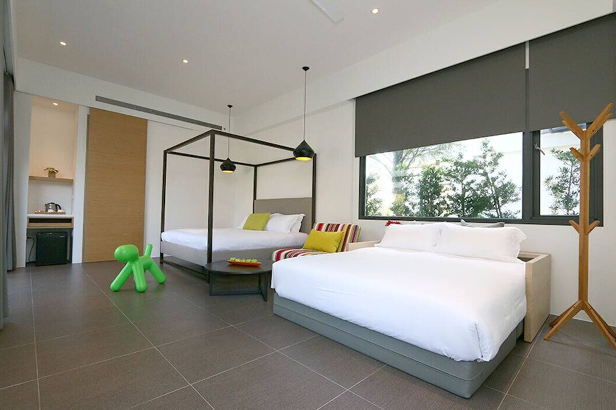 A modern bedroom with a large bed, a daybed, and a canopy bed. There is a small table with a chair, a green toy figure, and a coat rack.