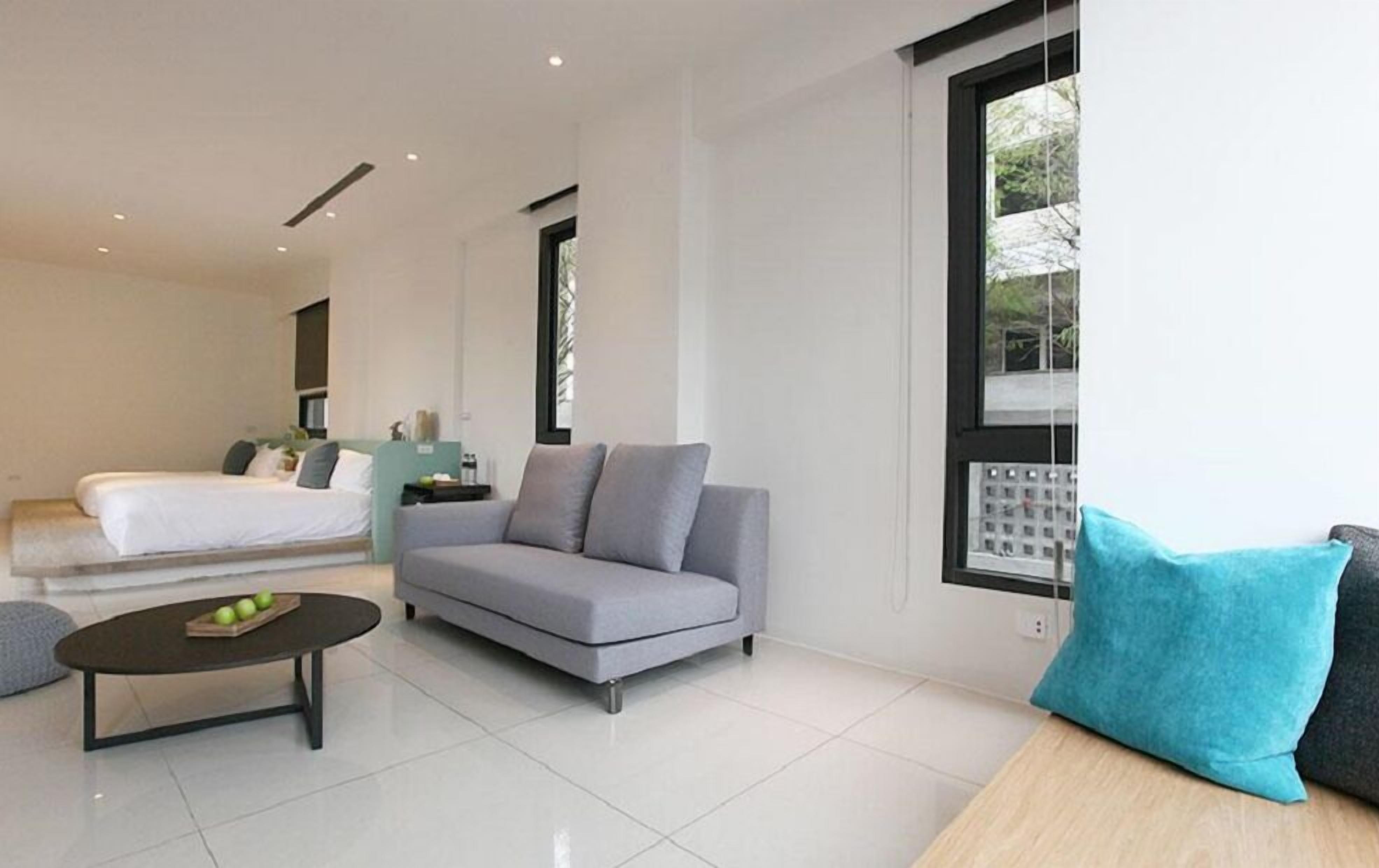 A modern hotel room with a bed, grey sofa, and a small table with apples.