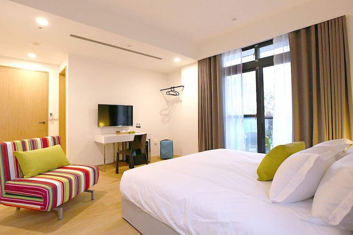 A hotel room with a bed, a desk, a television, and a colorful striped sofa.