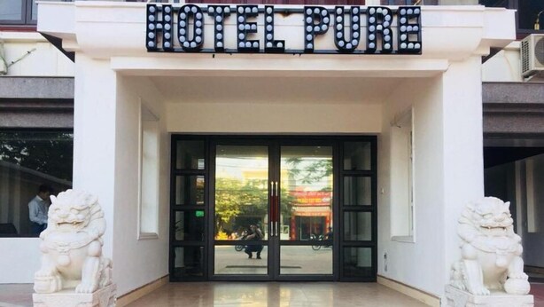 The entrance of a hotel with a sign reading "HOTEL PURE" above the doors, flanked by two lion statues. - Hotel Pure (Hai Phong)