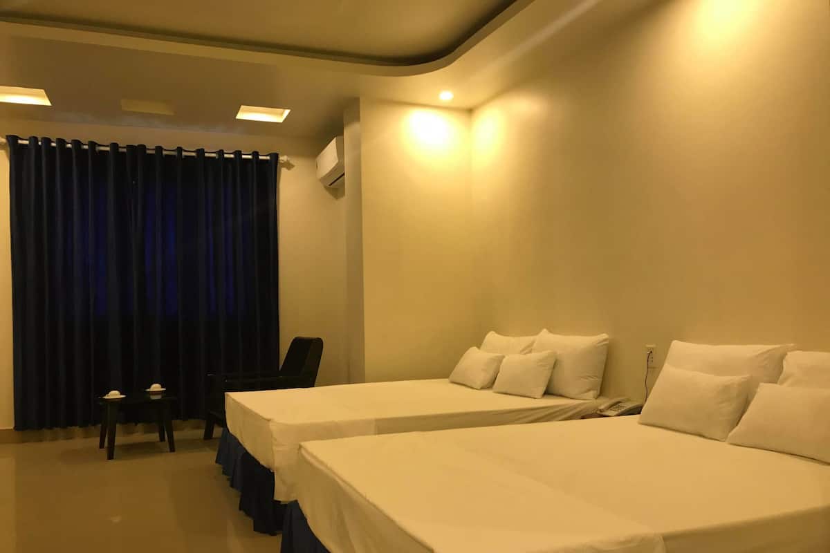 A hotel room with two single beds, a desk, a chair, and a curtain.