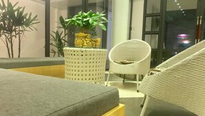 A modern hotel room with a grey sofa, wicker chairs, and a potted plant. - Hotel Pure (Hai Phong)