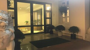 A modern entrance with glass doors, a black mat, and potted plants. - Hotel Pure (Hai Phong)