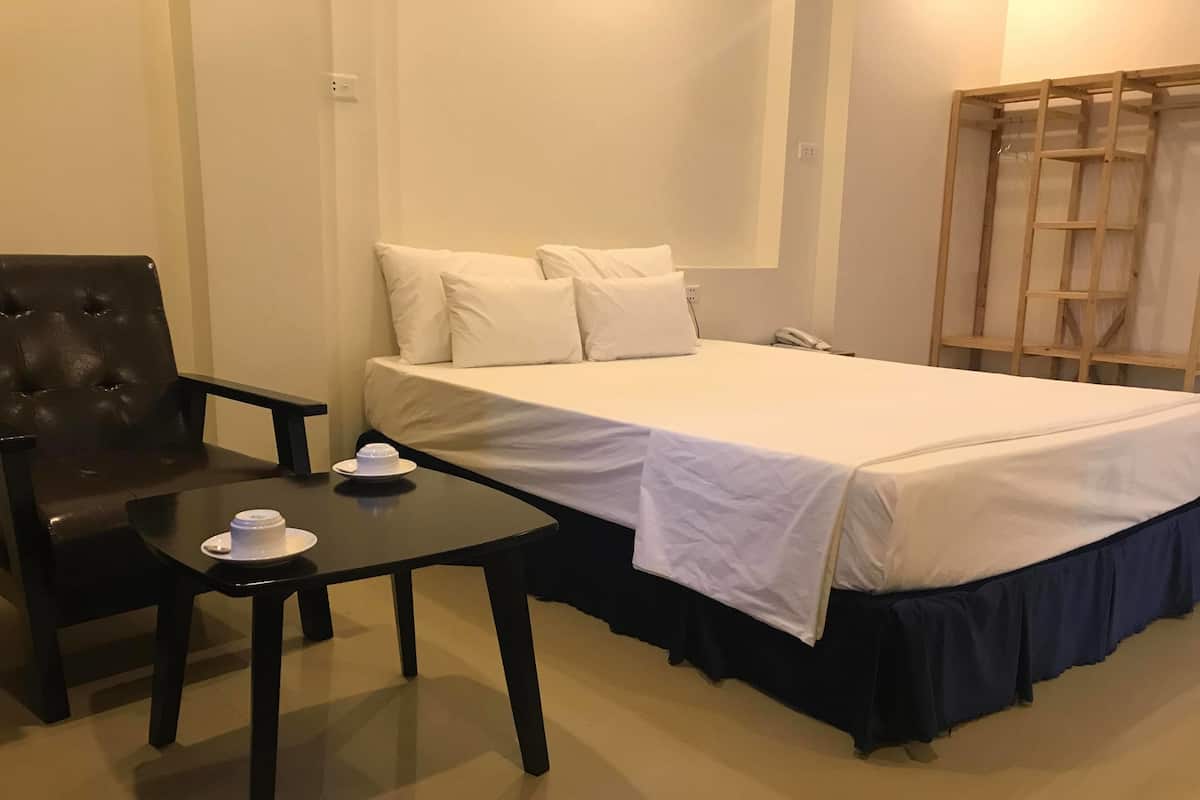 A hotel room with a bed, a chair, a small table with a cup and saucer, and a phone on the wall.