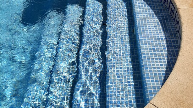 En swimmingpool med klart, blåt vand og en flisepier.