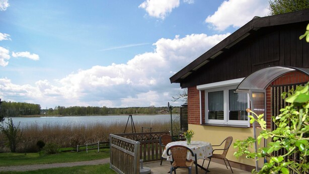 Een terras met tafel en stoelen met uitzicht op een meer, een houten hek en een gebouw met een raam.