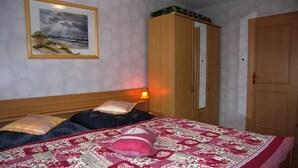 Een slaapkamer met een bed, kussens, een nachtkastje, een lamp, een garderobe en een lijst met een afbeelding aan de muur.