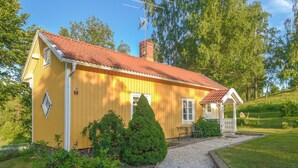 Una casa de madera amarilla con techo rojo, una chimenea y un pequeño porche con una mesa y sillas.