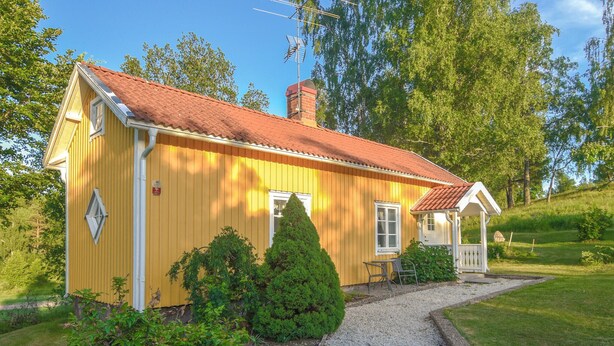 A yellow wooden house with a red roof, a chimney, and a small porch with a table and chairs. - Awesome home in åsensbruk with kitchen (Åsensbruk)