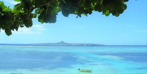 Un paisaje costero con aguas turquesas cristalinas, un pequeño barco y una montaña distante.