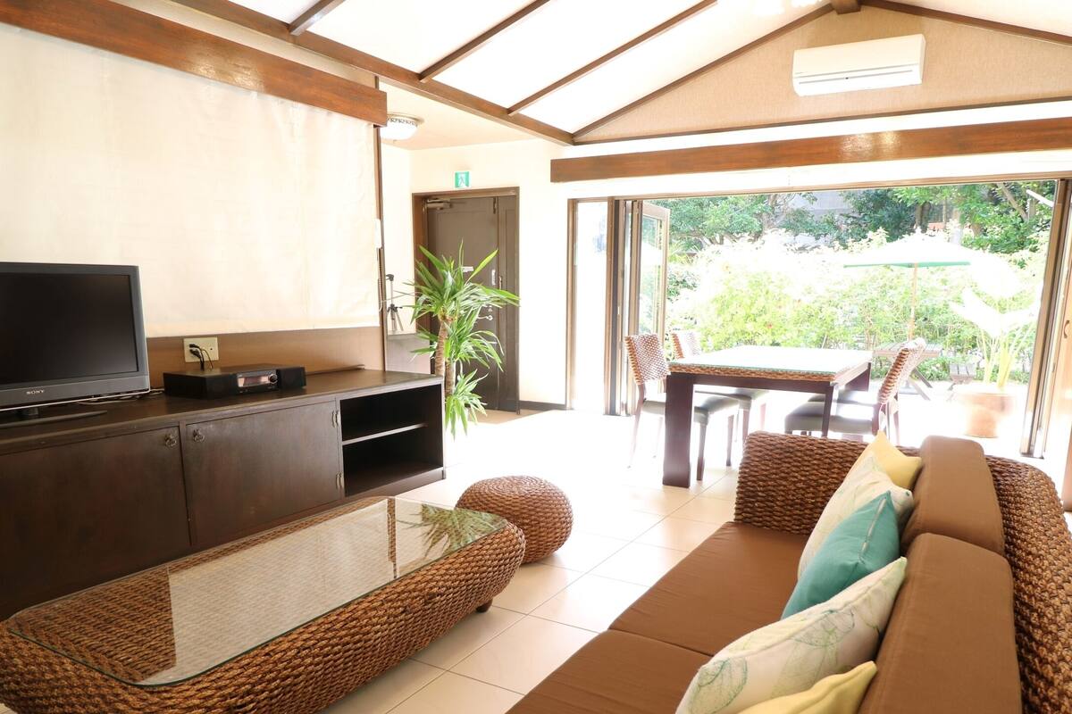 A modern living room with a flat-screen TV, wicker furniture, and a glass-top coffee table.