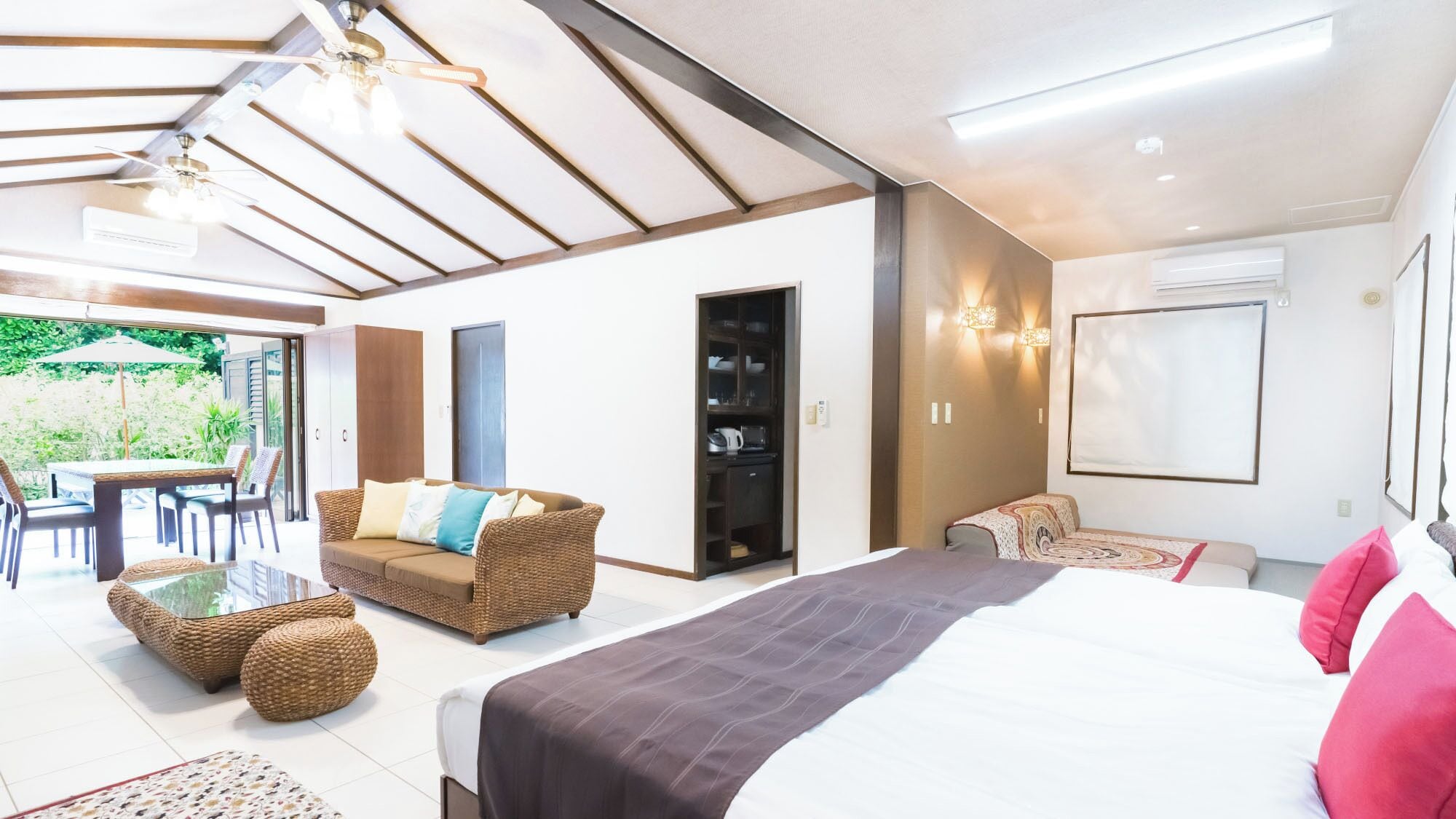 A bedroom with a bed, a sofa, a dining area with chairs, and a view of the outdoors.