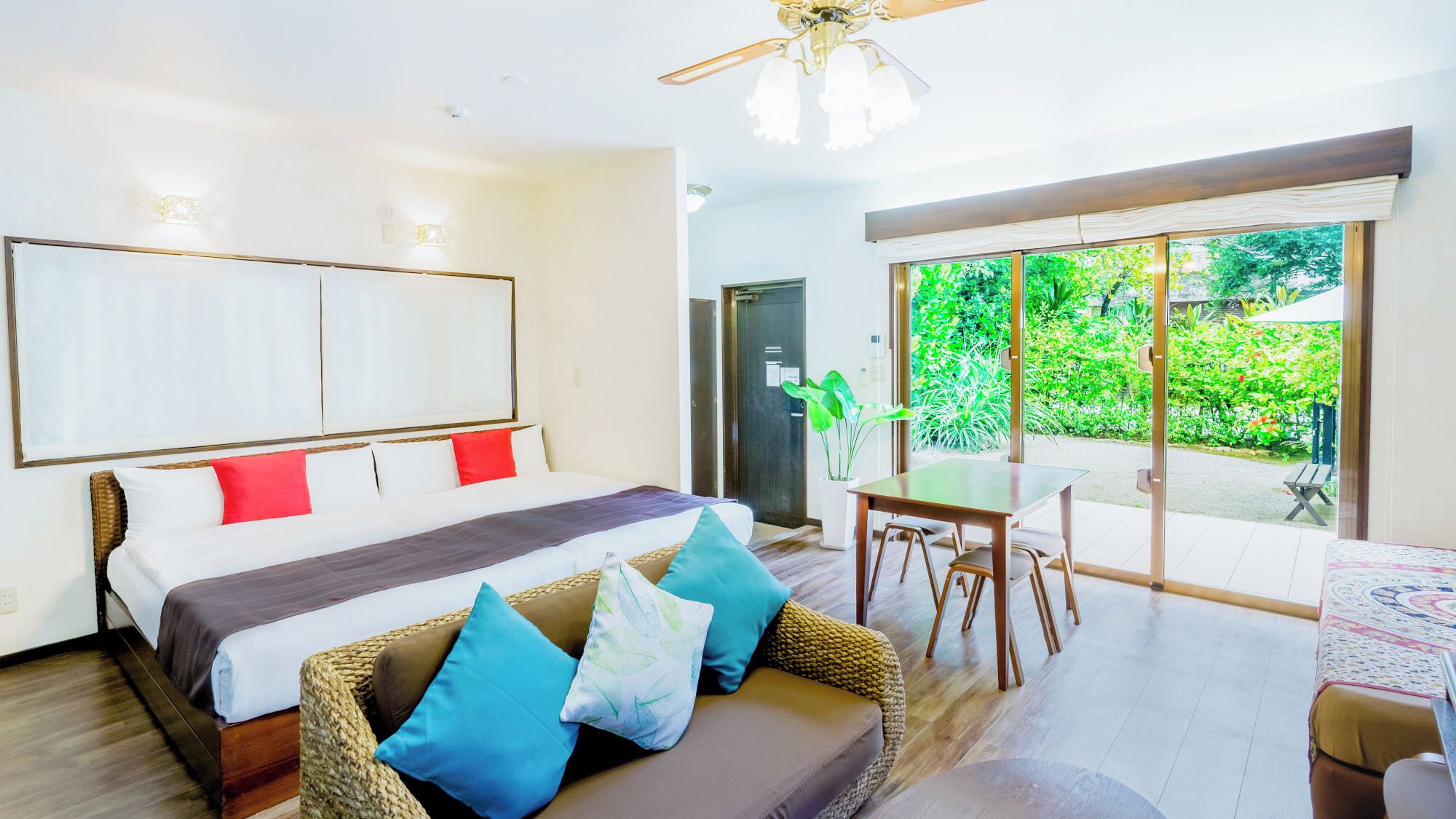 A bedroom with a bed, a sofa, a dining table, and a view of greenery outside.