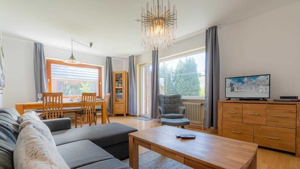 Un soggiorno moderno con divano, tavolo da pranzo, televisione e lampadario.