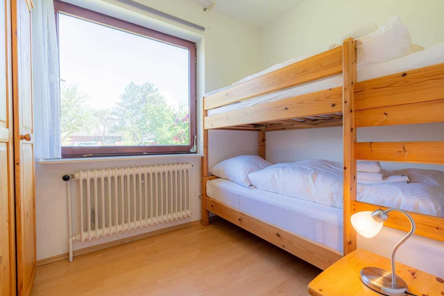 Een slaapkamer met een stapelbed, raam, verwarming en een bedlampje.