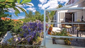 Eine Terrasse mit Gartenmöbeln, einem weißen Tor und violetten Blumen.