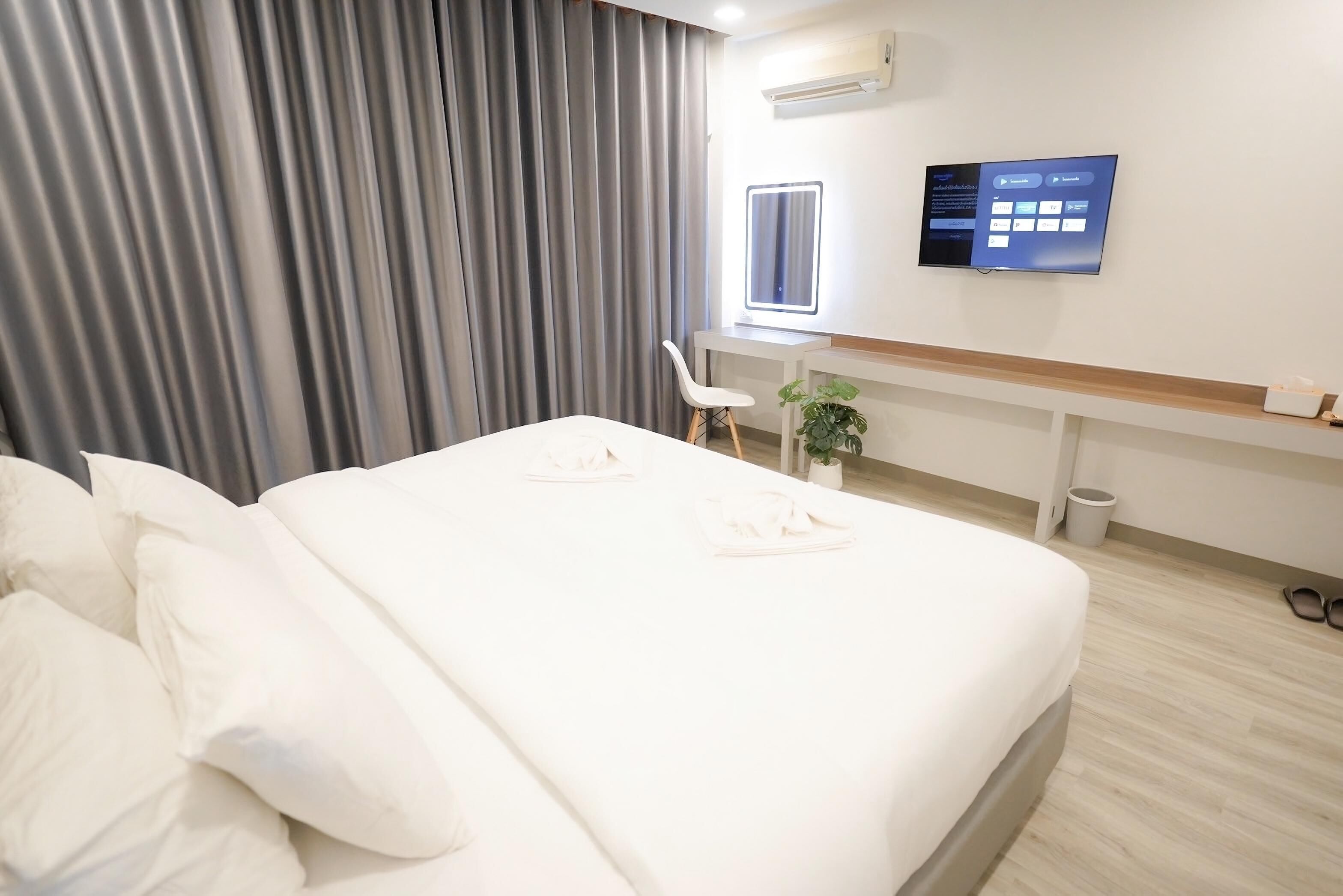 A hotel room with a neatly made bed, a desk with a computer, a chair, and a small plant.