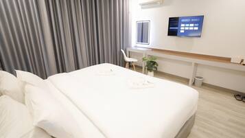 A hotel room with a neatly made bed, a desk with a computer, a chair, and a small plant.