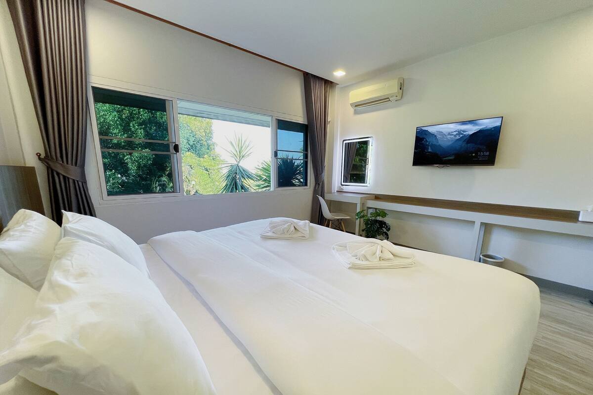 A hotel room with a large bed, two windows, an air conditioning unit, a TV, and a small desk.