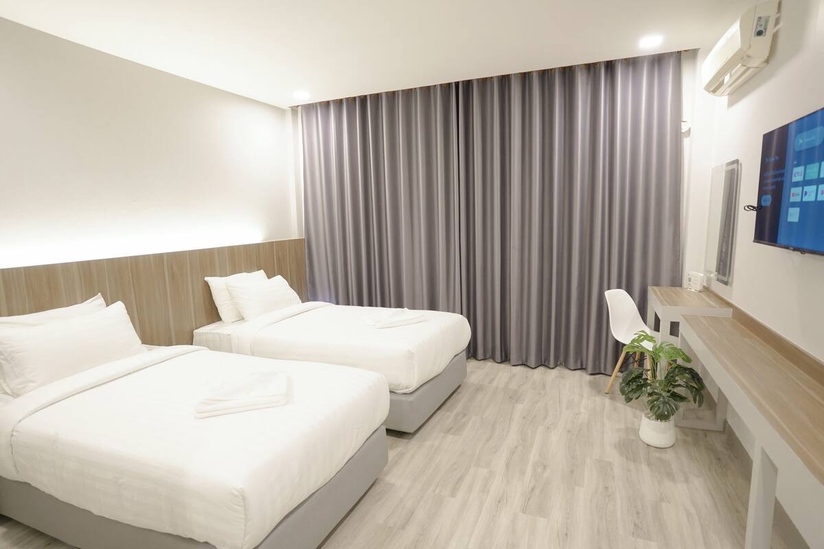 A hotel room with two beds, a desk, a chair, and a potted plant.