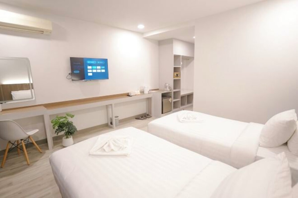 A hotel room with two beds, a desk, a chair, a TV, and a shelf with toiletries.