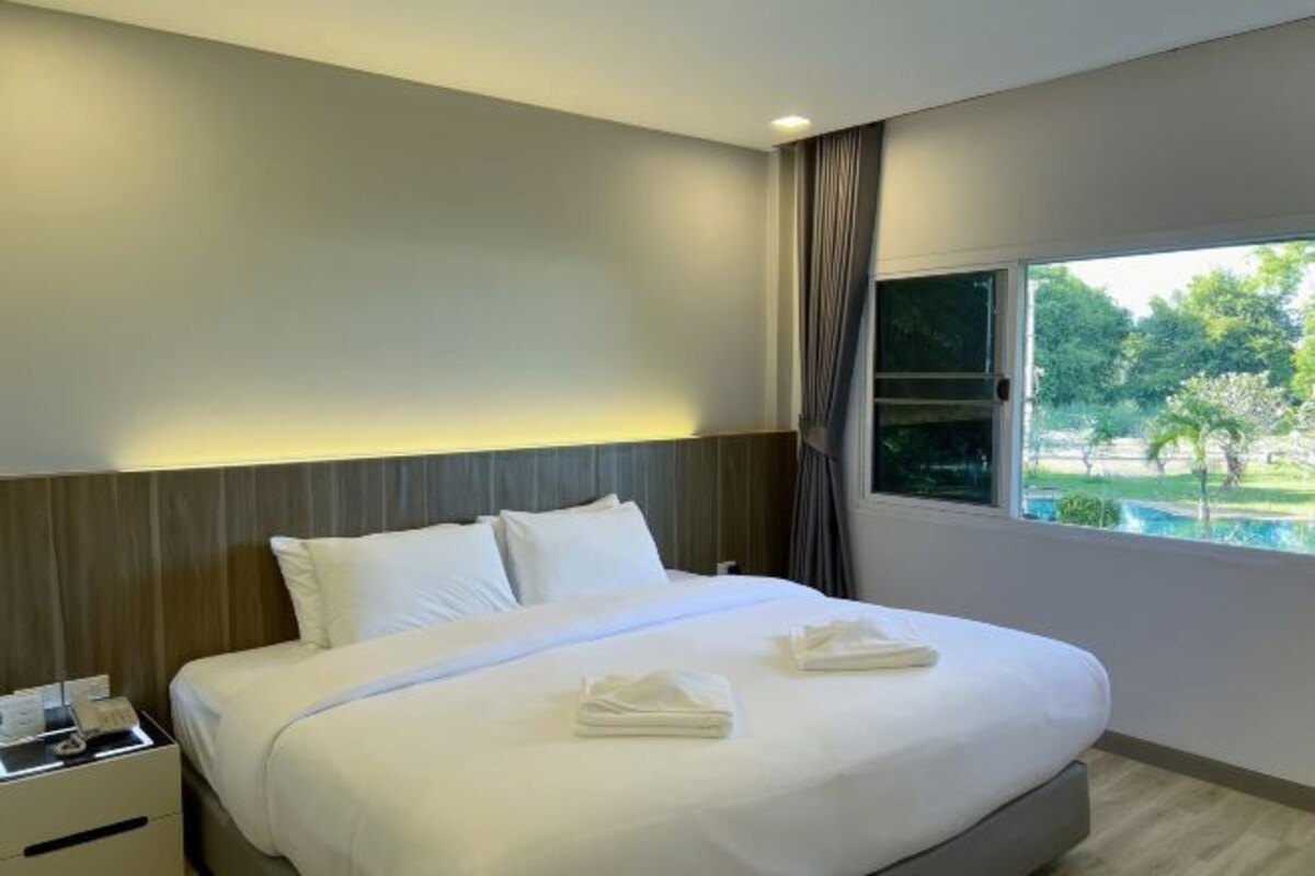 A hotel room with a large bed, a bedside table with a phone, and a window with a view of greenery.