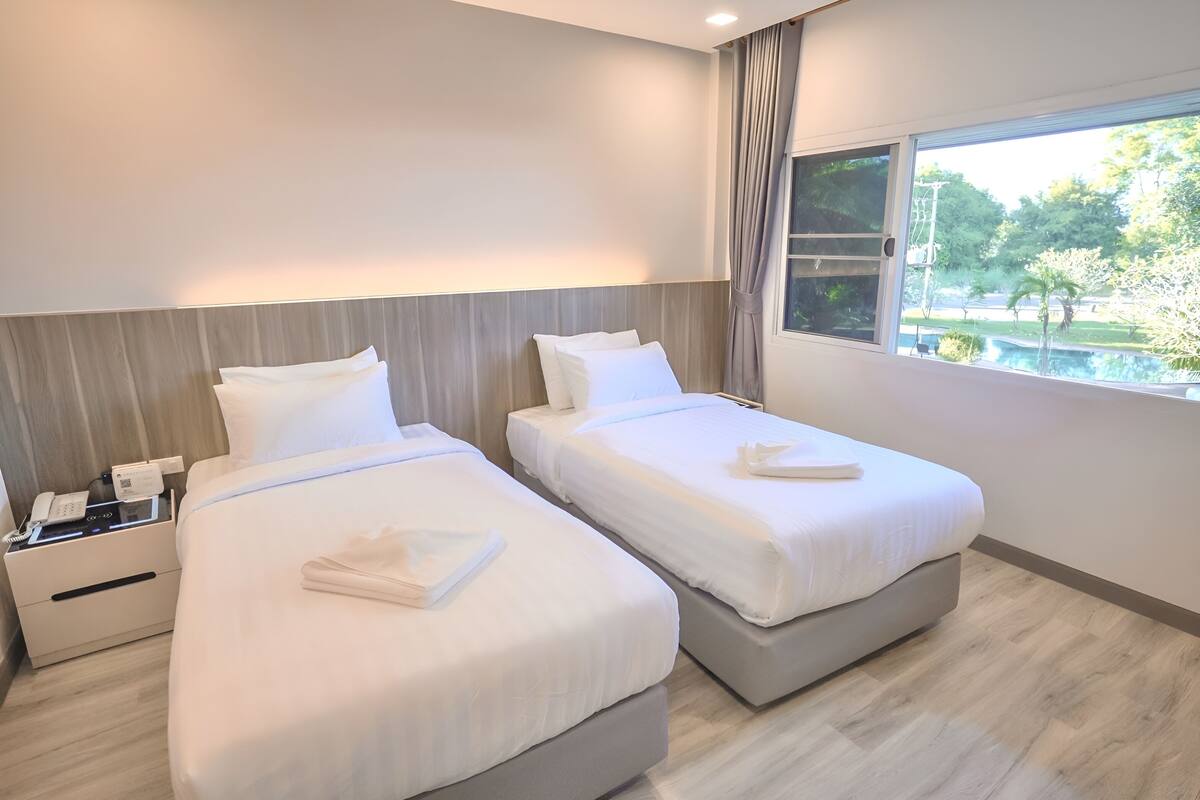 A hotel room with two beds, a bedside telephone, and a window with a view of a garden.