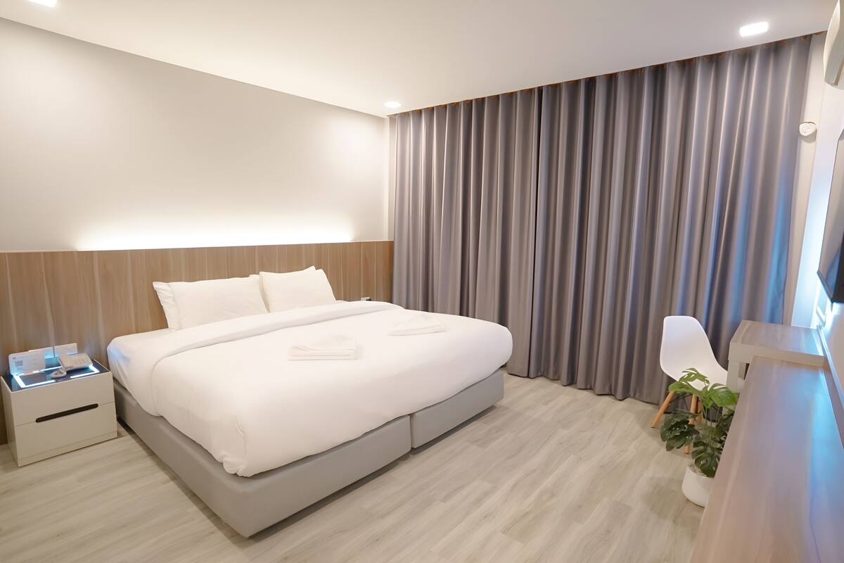 A modern hotel room with a large bed, bedside tables, a desk, and a potted plant.