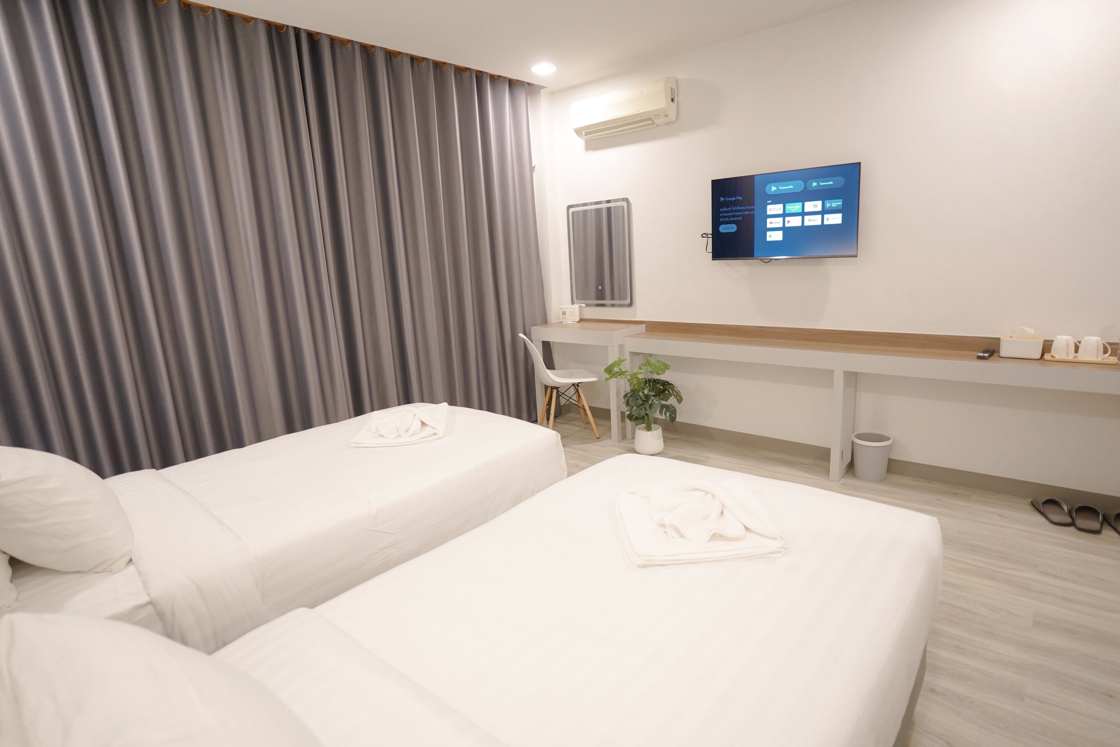 Habitación de hotel con dos camas, un escritorio, una silla, un televisor y una planta en maceta.
