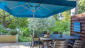 Une terrasse extérieure avec une table et des chaises, un parasol bleu et une enseigne sur laquelle on peut lire des mots comme « SABLE » et « PARADIS ».