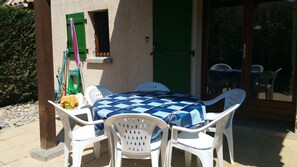 Un patio con una mesa cubierta con un mantel a cuadros, rodeado de sillas de plástico blancas.