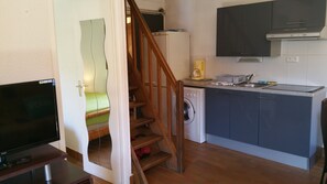 Una cocina compacta con lavadora, cafetera y un pequeño comedor con televisor.