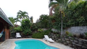 A swimming pool with two lounge chairs, surrounded by a stone patio and lush greenery. - Authentic and comfortable Martinique Villa with pool, 400m from the beach  (Sainte-Anne)