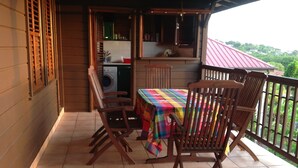 A wooden balcony with a tiled floor, a table with a colorful tablecloth, and wooden chairs. - Authentic and comfortable Martinique Villa with pool, 400m from the beach  (Sainte-Anne)
