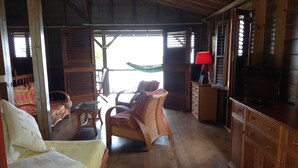 A wooden cabin interior with a bed, a wicker chair, a small table, a cabinet, and a television. - Authentic and comfortable Martinique Villa with pool, 400m from the beach  (Sainte-Anne)