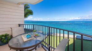 Un balcone con tavolo in vetro, sedie e vista sull'oceano.