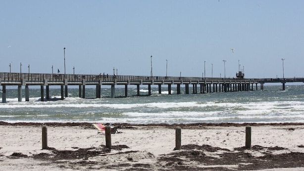 Um cais que se estende para o oceano, com uma praia de areia em primeiro plano.