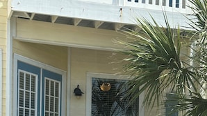 Uma casa com varanda branca, porta azul e um pequeno jardim.