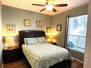 Un dormitorio con cama, dos mesitas de noche, ventilador de techo y ventana con persianas.