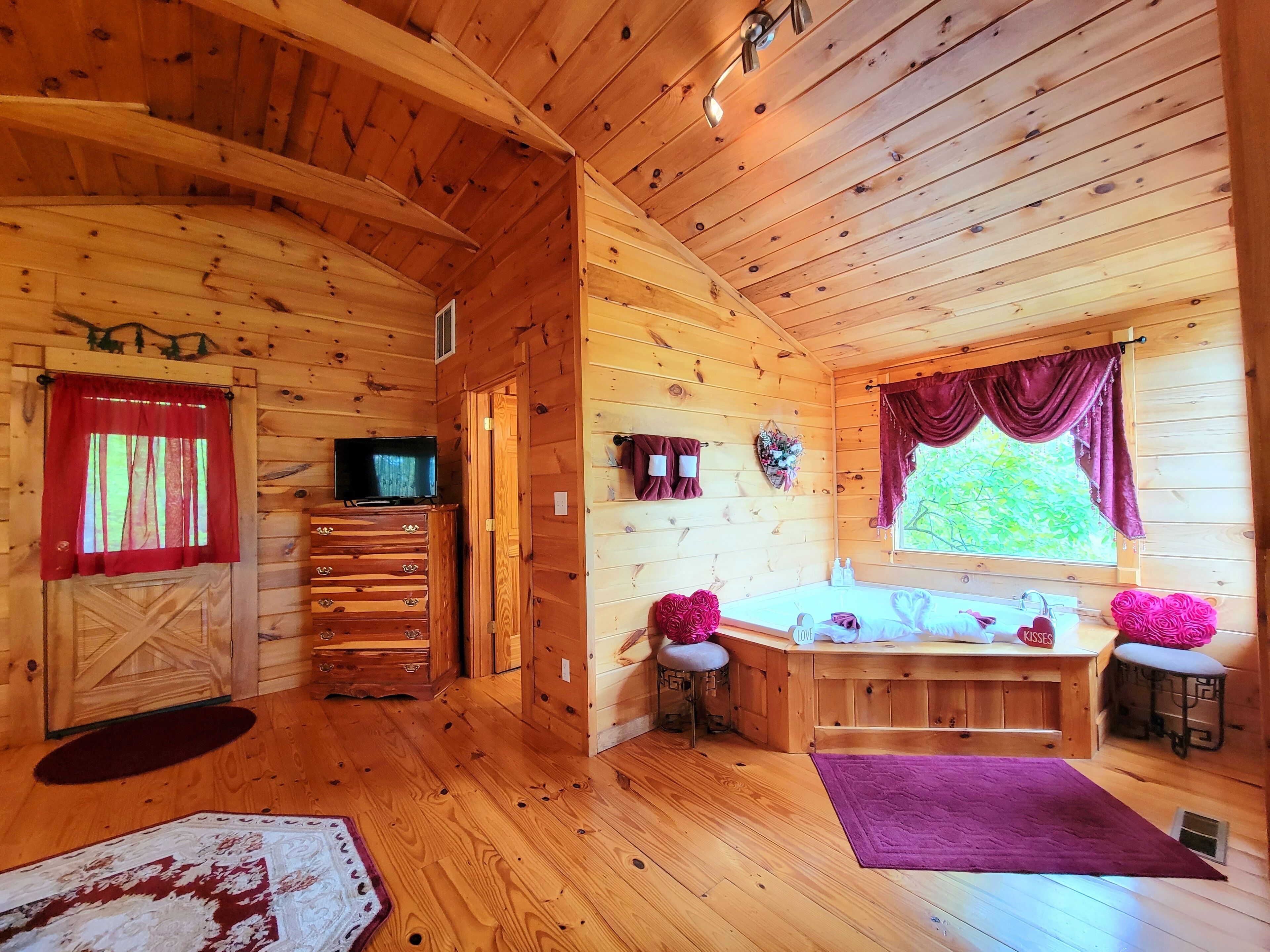 A wooden cabin interior with a TV, wooden dresser, vanity with sink, and a window with curtains.
