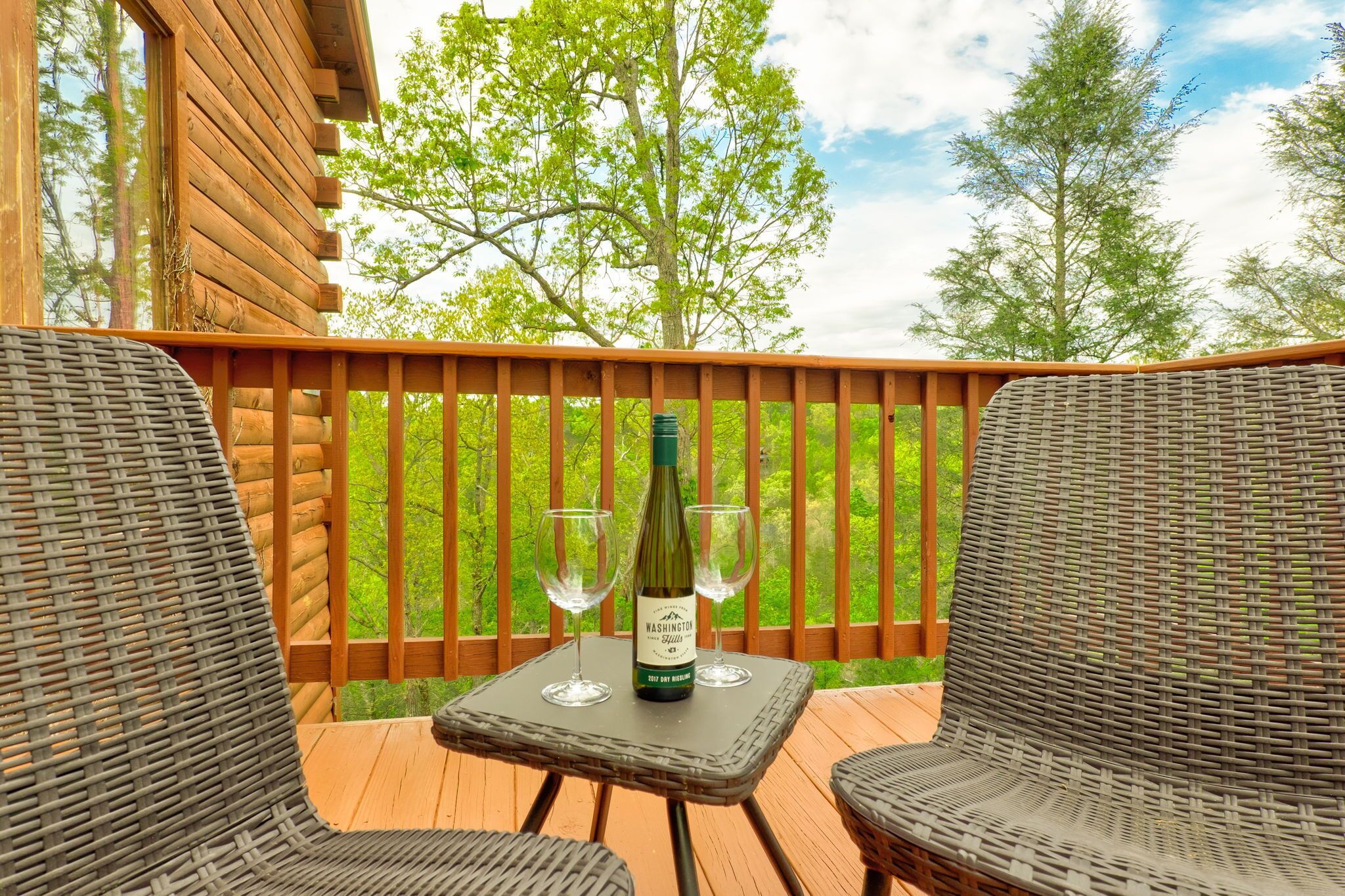 A wooden deck with wicker furniture and a bottle of wine on a table.