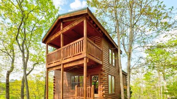A wooden cabin with a balcony, surrounded by trees.