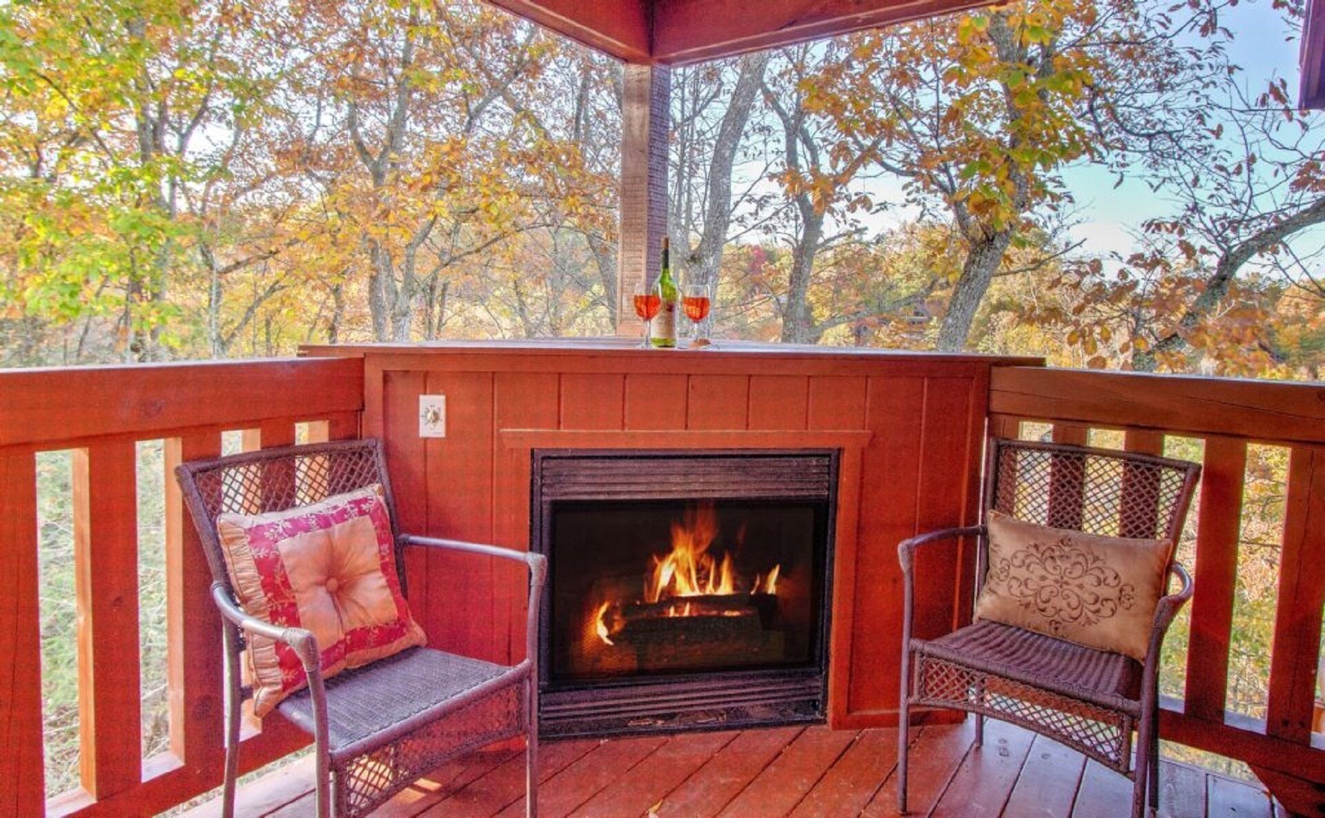 Une terrasse en bois avec un foyer, deux fauteuils en osier et une vue sur les arbres aux couleurs automnales.