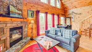 A cozy cabin interior with a stone fireplace, wooden walls, a blue sofa, and a dining area.