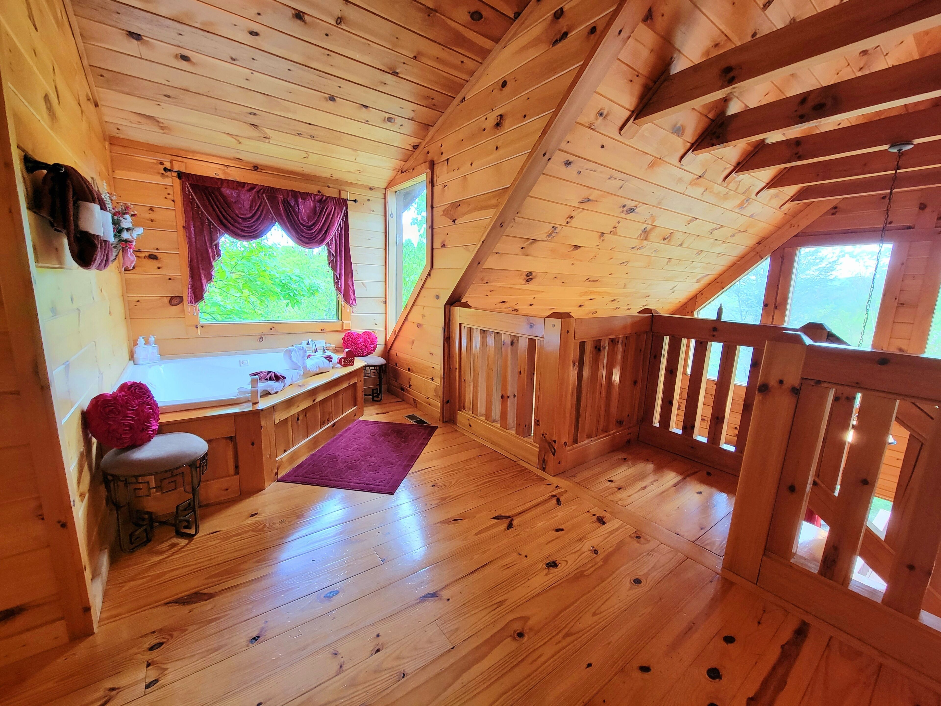 A wooden cabin interior with a kitchen area, a window with curtains, a wooden staircase, and a small stool.