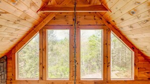 A wooden cabin with a pitched roof, large windows, and a view of a forest.