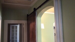 Un couloir avec une porte en bois, une porte blanche et un luminaire fixé au mur.